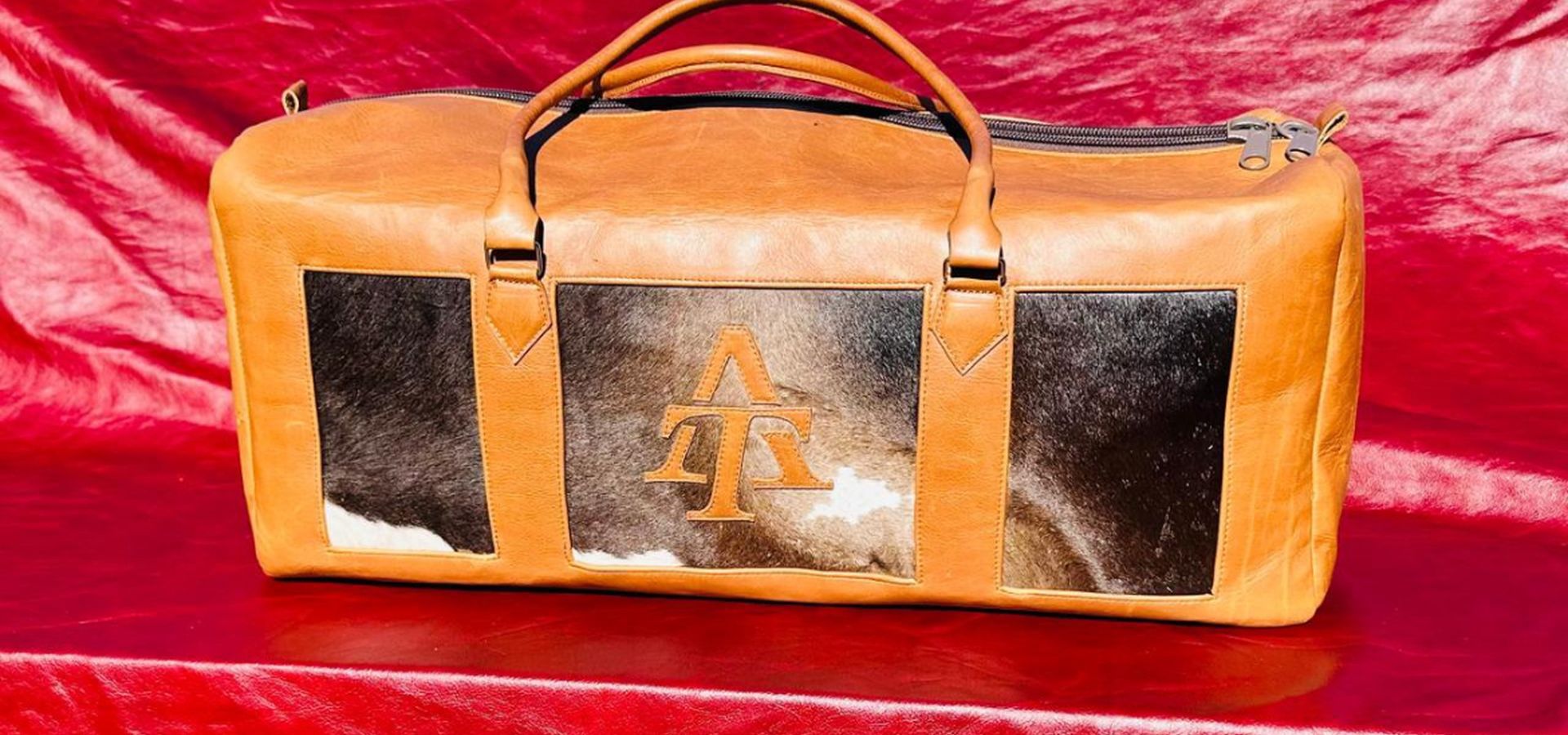 The AT Royal Travelex in tan with Nguni hide panels, photographed on a red drape