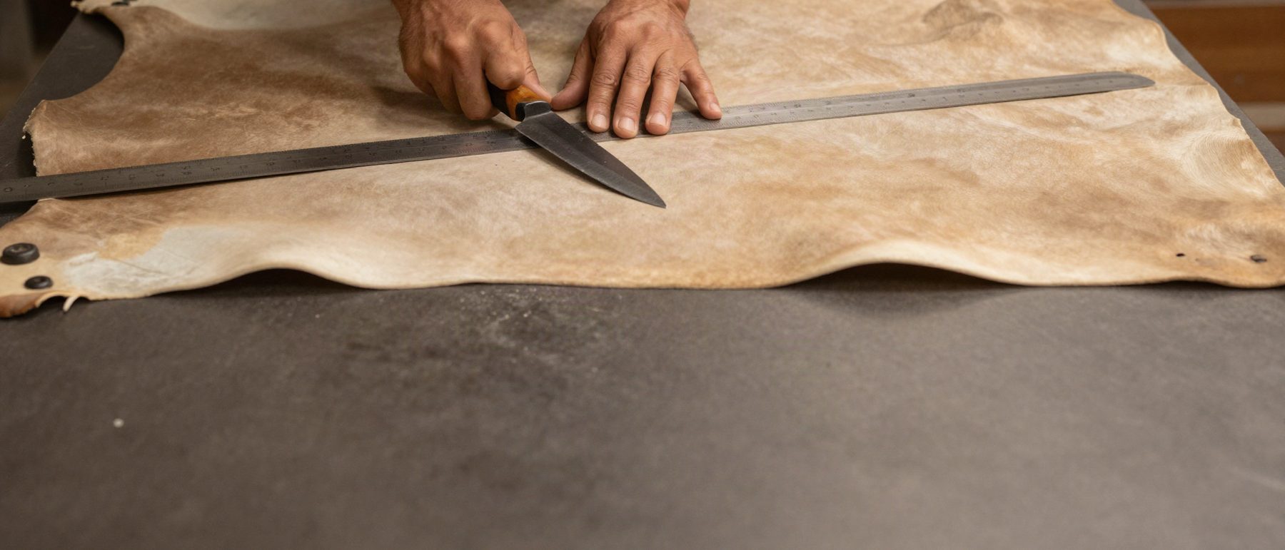 A hide being cut by hand against a steel rule on the cutting table