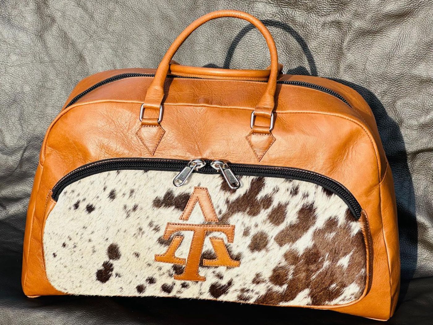 The AT Overnight Bag in tan, photographed three-quarter on, with six construction features called out
